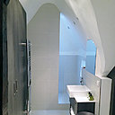 En continuité de la chambre, une salle de bains discrète a été aménagée. La douche aménagée dans une alcôve semi-ouverte, est partiellement cachée par un pan de mur carrelé, et les rangements offrent une unité esthétique. Au sol, les deux espaces se différencient.