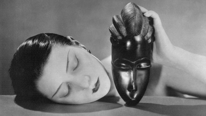 Publiée pour la première fois le 1er mai 1926 dans le Vogue français, sous le titre Visage de nacre et Masque d’ébène, elle apparait sous son titre définitif, en 1928. La chanteuse française Alice Prin, alias Kiki de Montparnasse, et modèle du photographe à partir de 1921, est représentée ici le visage allongé sur une table, tenant un masque africain de la main gauche. Si cette photographie joue sur le contraste des couleurs, les deux visages entrent pourtant en résonance, et semblent se répondre.