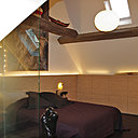 Délimitée par un mur en verre dépoli, la salle de bains ouverte fait partie intégrante de la chambre. Les couleurs chaudes et les lumières intégrées à la tête de lit qui se prolonge en rangement sous la pente de toit participent à l’ambiance tamisée et douillette de cette pièce.