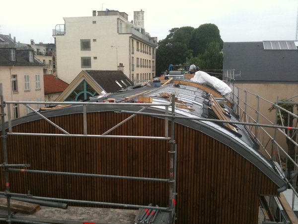 Le bâtiment rénové et surélevé a été recouvert d’une nouvelle toiture en forme de coque bateau retournée. Une toiture en zinc, idéale pour former une belle courbe. Un matériau fortement recommandé à Versailles.