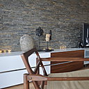 On se croirait dans un living-room américain des années 1950 ou 1970, dans une villa à Los Angeles ! Au- dessus d’une enfilade de buffets de style contemporain (Cinna), le mur est tapissé d’un appareillage de pierre naturelle (briquettes assemblées sur plaquettes, avec effet de relief, Porcelanosa). Fauteuil vintage des années 1930.