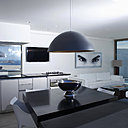 La cuisine graphique est meublée d’une grande table en granit noir, conçue en deux parties. Un second plateau permet de prendre ses repas à l’extérieur. Un salon immaculé s’ouvre sur la piscine. Suspension lumineuse avec intérieur en métal doré à la feuille, Via Manzoni.