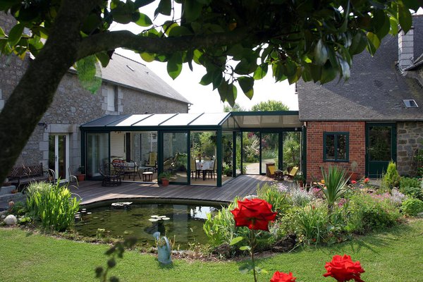 Une véranda peut répondre à différentes besoins. Ici, elle est à la fois utile et agréable, faisant office de liaison entre les deux bâtiments. Elle côtoie les pièces de vie tout en discrétion, s’intégrant harmonieusement dans l’ensemble architectural.