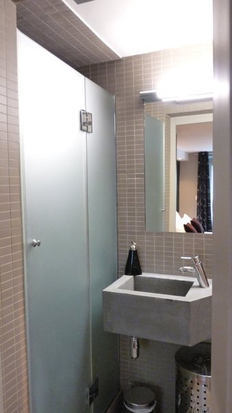 Dans cette micro salle de bain (2 m²), la vasque en béton a été réalisée sur mesure, avec un pan coupé, pour dégager un passage vers le coin toilettes.