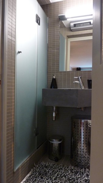 Le robinet a été installé, latéralement, pour ne pas gêner la circulation. La cabine de douche biseautée, à pan coupé,  permet d’épouser l’espace sans perdre de place. Carrelage en grès cérame, Winckelmans.