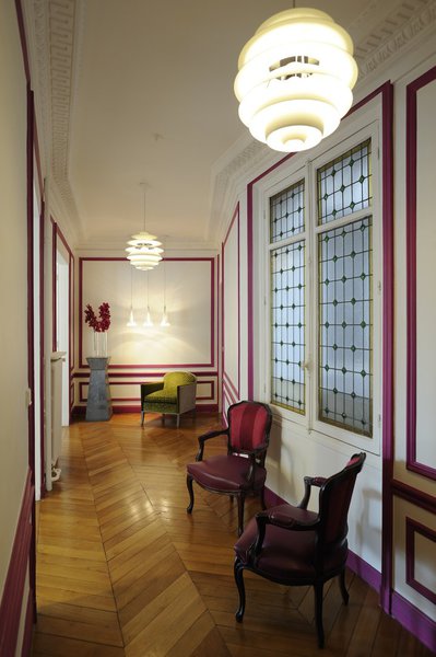 L’entrée, façon couloir, qui dessert toutes les pièces est animée et rendue plus accueillante par un apport de couleur. Les moulures des murs ont été peintes en rouge framboise pour faire oublier leur côté trop classique. Les fauteuils anciens ont été retapissés dans des tissus aux tons vifs.