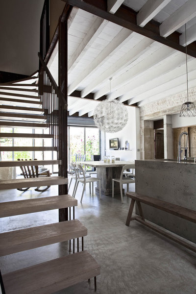 La poutraison a été peinte en blanc. L’escalier en bois et métal suspendu aérien s’accroche au mur en terre et sable.