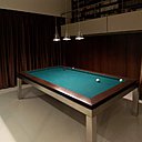 Le billard a été placé à proximité de la bibliothèque, située en hauteur et à laquelle on accède par le biais d’une passerelle. Les rideaux cachent les baies vitrées de l’entrée principale, pour favoriser la circulation vers le patio.