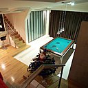 Le billard est encadré par un emmarchement, et repose sur un sol en résine qui contraste avec le plancher. La porte en acier et verre opalescent, d’esprit industriel, mène à la buanderie, à l’arrière cuisine et aux toilettes.