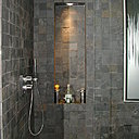 Appart 1. La douche est tapissée avec  un carrelage en pierre, intégrant dans sa composition du métal oxydé.