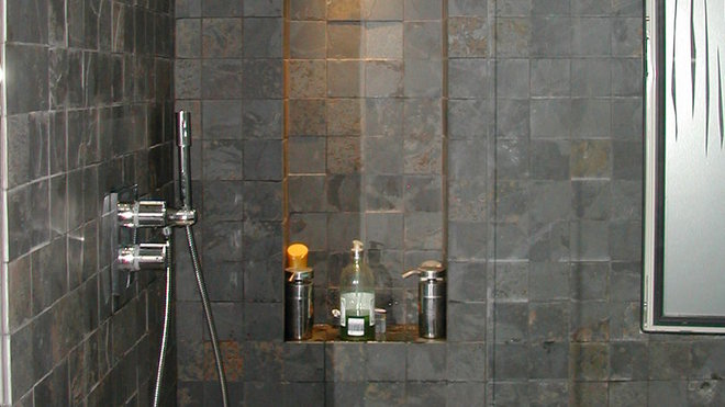 Appart 1. La douche est tapissée avec  un carrelage en pierre, intégrant dans sa composition du métal oxydé.