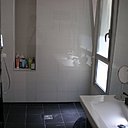 Appart 2. Carrelage et vasque immaculée brillante, receveur carrelé sombre et mat pour un effet bicolore et contrasté dans la salle de bains.