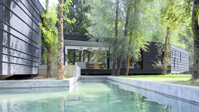 Décollée du sol et en porte-à-faux, sur un étang, elle se glisse entre les arbres sans qu’aucun n’ait été sacrifié. Un jeu de cloisons vitrées mobiles rend l’espace fluide, et autorise le bassin à carpes et à nénuphars à pénétrer jusque dans les pièces de vie. Cette maison écologique en ossature bois avec façade en zinc pré-patiné et verre, est construite sur une dalle béton avec utilisation de l’acier pour le porte-à-faux. Création If Architecture [Jean-Marie Pettès], Maison Serpentine à Lavaur (81), 2011.