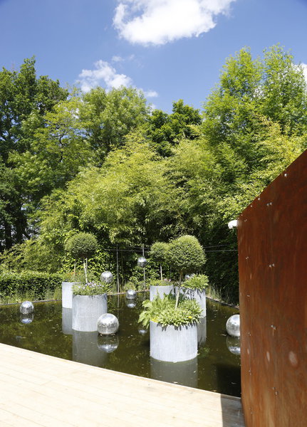 En apesanteur. Un sas d’isolement en métal patiné de rouille isole le jardin de la frénésie extérieure. De petites ouvertures à hauteur d’œil éveillent la curiosité du promeneur, qui peut se lover, une fois l’antichambre franchie, dans un des fauteuils ornés de pictogrammes illustrant les 5 sens. Création Mathieu Brison, Luc Voisin et Jeanne Couaillier (France).