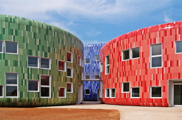 Ce centre d’éducation pour les enfants, situé à Valence, est constitué de blocs cylindriques dont les façades sont recouvertes de céramique. Ce matériau durable est l’une des clés de ce projet de construction d’un bâtiment écologiquement responsable, également équipé de panneaux solaires. Les teintes des carreaux de céramique varient en fonction de la luminosité.