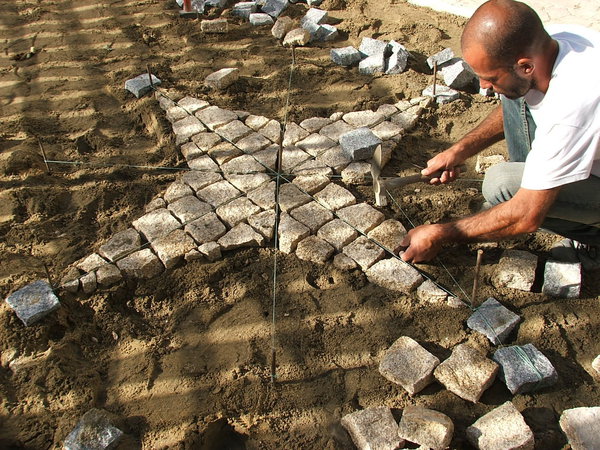Etape 11 : Réaliser le pavage de la petite étoile avec des pavés entiers à l’intérieur de la forme, et avec des pavés taillés sur le pourtour de cette dernière. Il s’agit d’enfoncer les pavés dans le sable cimenté, tout en gardant une hauteur la plus régulière possible entre les pavés de granit.