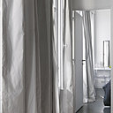 Dans la chambre, on a choisi un sol en béton ciré. Dans le salon, le sol est nappé d’un parquet en chêne vieilli, chez Décoplus Parquet. Les rideaux en taffetas de soie déclinent le gris et le blanc avec un effet de rayures.