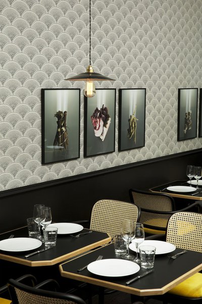 L’atmosphère intimiste des tables est apportée par le soubassement laqué en noir,  le papier peint japonisant et les touches de jaune sur les fauteuils en cannage.