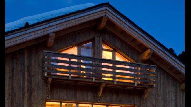Un chalet à la façade percé d’une baie vitrée qui magnifie par la vue panoramique sur la montagne.
