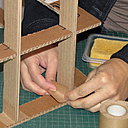 Etape 13. Posez la plaque 1 sur le plan de travail. Couchez la structure dessus. Fixez la structure à la plaque 1, grâce à des morceaux de kraft gommé collés en angle entre chaque traverse et ladite plaque 1. Faites de même avec la plaque 3.