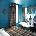 Dans la chambre « Forêt Enchantée », bleue, l’intérieur de la baignoire (Aquamass) s’illumine et le carrelage est composé d’une mosaïque irisée qui décline les couleurs de l’arc-en-ciel (Porcelanosa). Vasque bicolore en forme de bol, Aquamass. Double fonction, le miroir fait aussi office de télé.