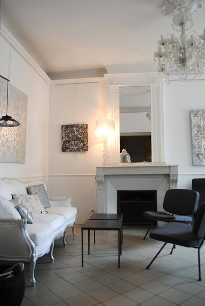 Chaises de Pierre Paulin noires et banquette Louis XV à la structure restaurée à la feuille d’argent, pour ce salon réservé aux hôtes. Cheminée en faux marbre et tableaux qui reprennent l’harmonie des couleurs de la pièce.