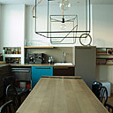 Dans la cuisine, une grande table familiale au plateau en chêne, rythmé par deux bandes d’acier en diagonale qui reprennent le dessin du piétement. Des chaises dépareillées, harmonisées par la même couleur noire, l’encadrent.