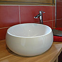 Dans la salle de bains des chambres d’hôtes, on retrouve le même code couleur, avec un carrelage rutilant qui s’associe à la chaleur du bois et la pureté immaculée d’une vasque en céramique à la forme organique.