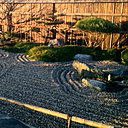 L'ensoleillement du jardin minéral crée des ombres sur la palissade, et révèle le gravier ratissé symbolisant des vagues s'écrasant contre des îles.