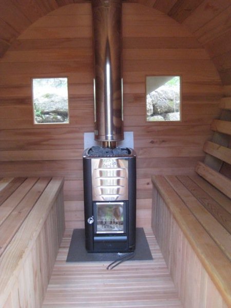Le sauna en bois est chauffé grâce à un poêle à bois à l’esthétique moderne et soignée.