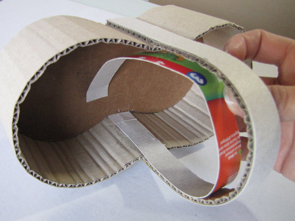 Etape 7 : Renforcez l'anse en collant, à la colle chaude, la bande de carton gris de 32 cm x 2 cm sur le côté extérieur de l'anse. De même, collez la bande de 29,5 cm x 2 cm sur le côté intérieur de l'anse.