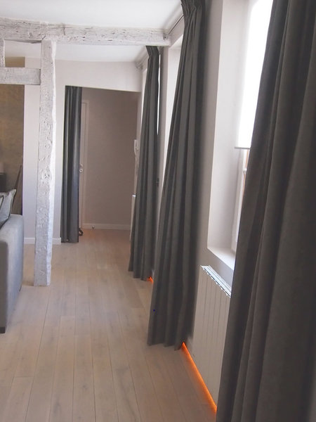 Les fenêtres sont habillées de rideaux gris (tissu Pierre Frey) qui font écho aux canapés du salon attenant. Un ruban de Leds balise le sol, sous les fenêtres, et accompagne les déplacements.