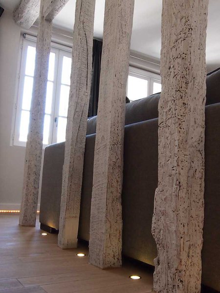 Derrière le canapé, au niveau du sol et à la base des poutres, des spots encastrés dans le parquet éclairent l’espace avec une douce élégance.