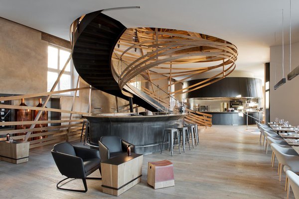 Au pied de l’escalier dans la brasserie, l’espace lounge et son bar en inox patiné, en forme d’ellipse, le mobilier en bois et cuir réalisé sur mesure évoquent l’authenticité de l’univers équestre. On aperçoit des fûts de bière traditionnels en cuivre.