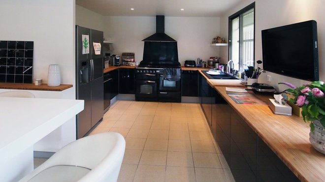 La zone de préparation des repas de la cuisine, de couleur noire, joue l’effet de contraste graphique avec le reste de l’espace nappé de blanc. Le plan de travail, en bambou, fait écho au dessus du buffet.