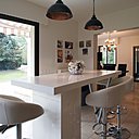 Librement inspirée d’une table réalisée par Le Corbusier pour la maison La Roche, cet îlot en Corian ® et acier offre un espace repas, un plan de travail supplémentaire et un rangement caché dans son piètement.