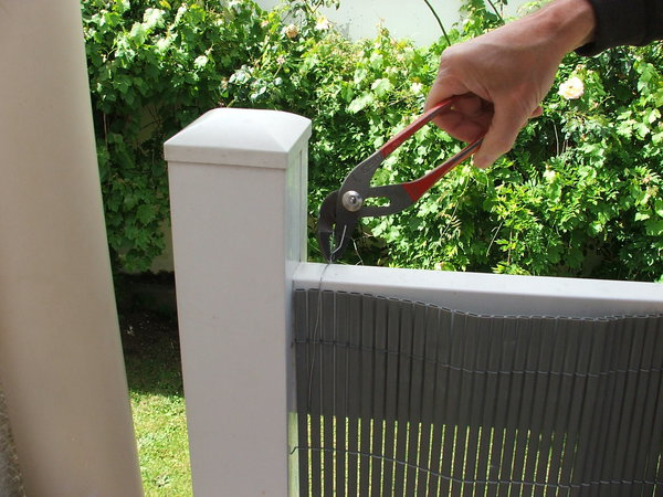 Etape 4 : Après avoir déroulé et plaqué la canisse sur la balustrade, passer le fil d’acier de fixation  au travers de la canisse et venant enrouler la traverse de la balustrade. A l’aide d’une pince multiprise, tirer les deux extrémités du fil d’acier et effectuer plusieurs rotations afin d’enserrer la fixation. Répartir les liens de fixation tous les 40 centimètres environ.