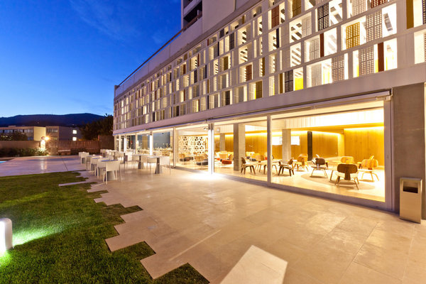 Le soir, la façade s’illumine, les larges baies vitrées laissent libres les salons de réception, sans rupture avec le dehors.