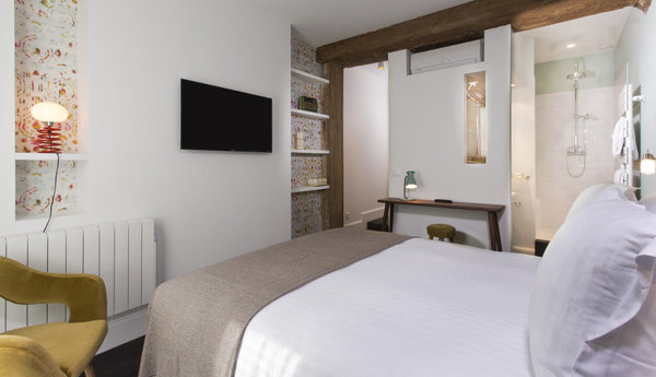 Vous trouverez dans la chambre Printemps une déco très naturelle avec des poutres apparentes et un papier-peint aux touches colorées sur fond blanc.