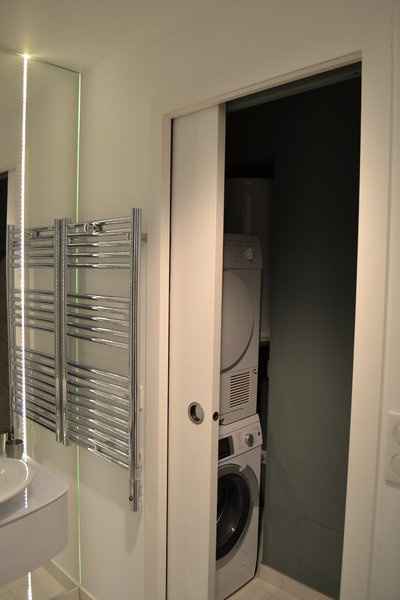 A droite du lavabo, un petit renfoncement a été optimisé pour créer une petite buanderie, cachée derrière une porte coulissante. Elle renferme discrètement lave-linge et sèche-linge.