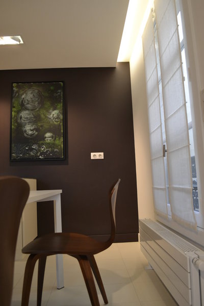 Dans la cuisine, harmonie en blanc et brun. Les chaises en bois teinté qui accompagnent la table de repas s’accordent avec la couleur chocolat du mur recouvert de Paperstone®.