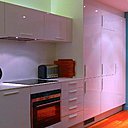 La cuisine se dévoile dès l’entrée, figurée par un mur peint en bleu et une grande affiche  de cinéma. Ses éléments discrets se confondent avec l’espace nappé de blanc.