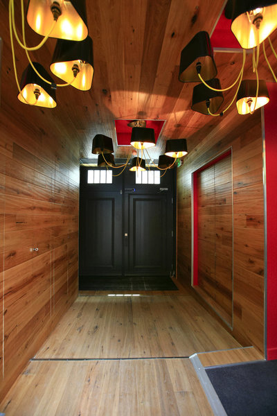 Le hall convivial est un écrin de bois. Tapissé du même matériau, sa teinte plus foncée, aux murs et au plafond, provient du traitement anti-feu réglementaire qui nécessite des couches supplémentaires de vernis. Au sol, le chêne a simplement été huilé. Luminaires, création Design Heure.