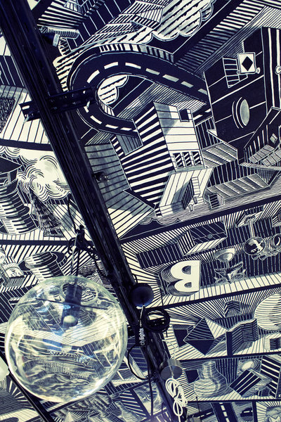 Le dessin du plafond prolonge la verrière d’origine située dans la deuxième partie du local jusqu’à la rue. Il est peint par le street artiste Douroune.