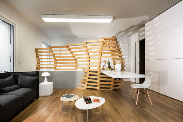 Une structure ajourée en hêtre intégrée à un meuble bas et une la table de repas sépare le coin salon et occulte la cuisine.