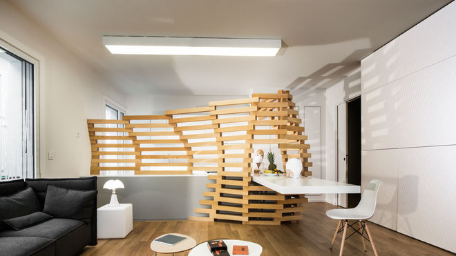 Une structure ajourée en hêtre intégrée à un meuble bas et une la table de repas sépare le coin salon et occulte la cuisine.