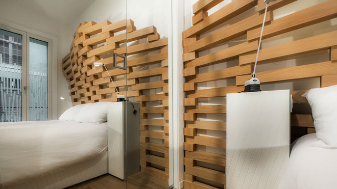 Dans la chambre, la structure ajourée joue le rôle de tête de lit, sa forme, décuplée par le miroir, offre son volume à l’espace. Les tables de chevet intégrées font écho aux meubles de la pièce de réception.