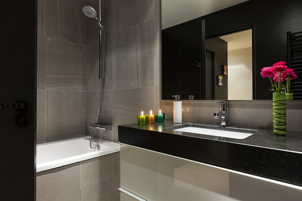 La salle de bains la plus spacieuse est accessible de la chambre du fils et sert aussi à sa mère. Les murs sont revêtus d’un carrelage de grès cérame imitant la pierre. Le meuble sous vasque (Ikea) est recouvert d’un plan en granit adossé à une crédence en faux-cuir.