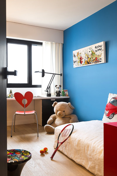 La chambre du fils Charles est caractérisée par un mur peint en bleu issu de la célèbre gamme de référence Pantone® (Tollens). Un long plan de travail supporté par des caissons noir et blanc (Ikea) fait office de bureau sur une longueur de 2,60 m. Les rideaux ont été accrochés à l’aide d’une tringle plate sous le caisson intérieur qui sert de coffrage aux volets roulants.