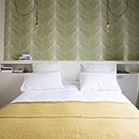 La chambre des parents est personnalisée par un papier-peint (Osborne & Little) en tête de lit, qui donne de la profondeur à l’espace. Le lit est encadré de deux niches et d’une tablette supérieure. Dessus de lit, Caravane.